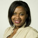Smiling Black woman with shoulder-length dark hair, wearing a beige button-up shirt, posing against a plain background.