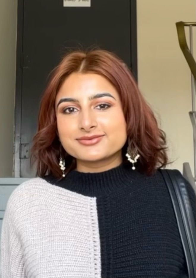 A woman with red hair is wearing a black and white sweater and earrings.