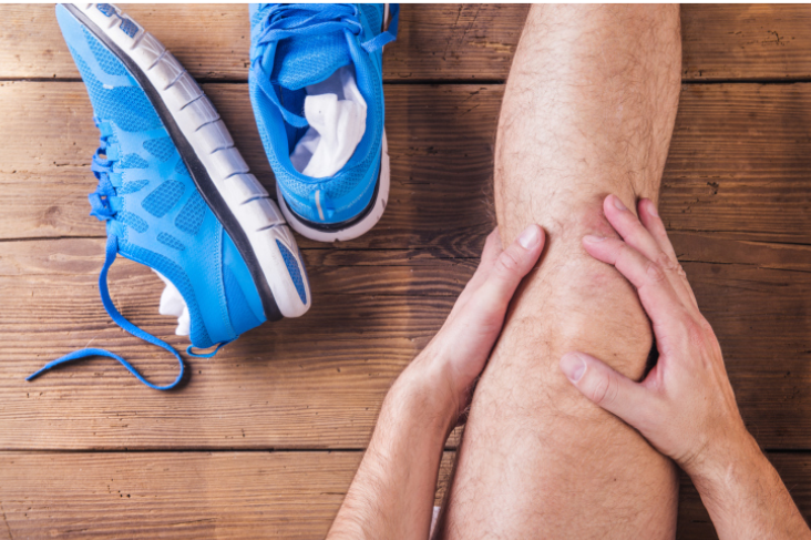 A person is holding their knee with a pair of blue shoes in the background.