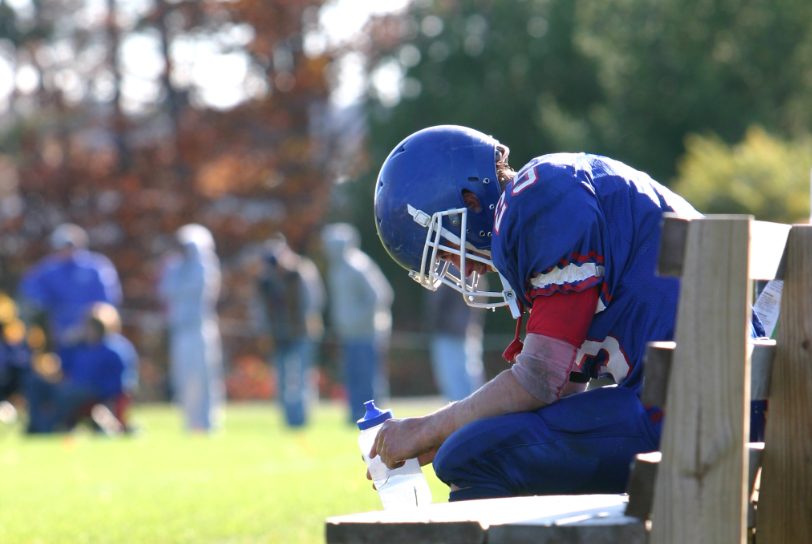 A football player in a blue uniform is kneeling on a bench