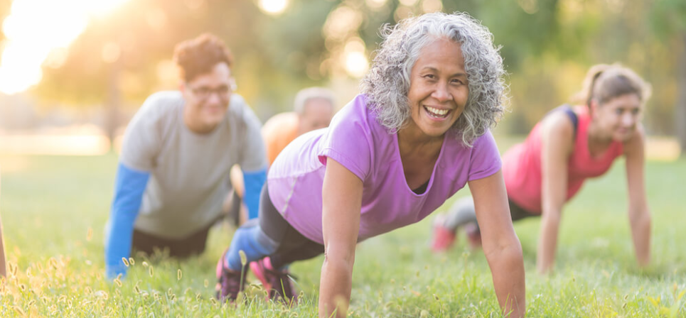 A group of people are doing push ups in the grass in a park.