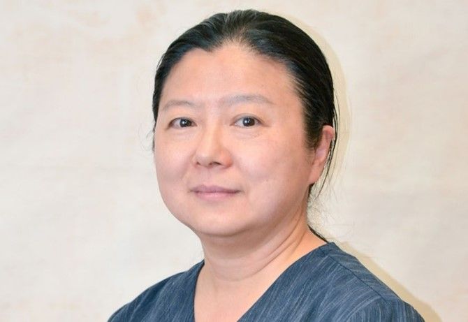 A woman in a blue scrub top is smiling for the camera.