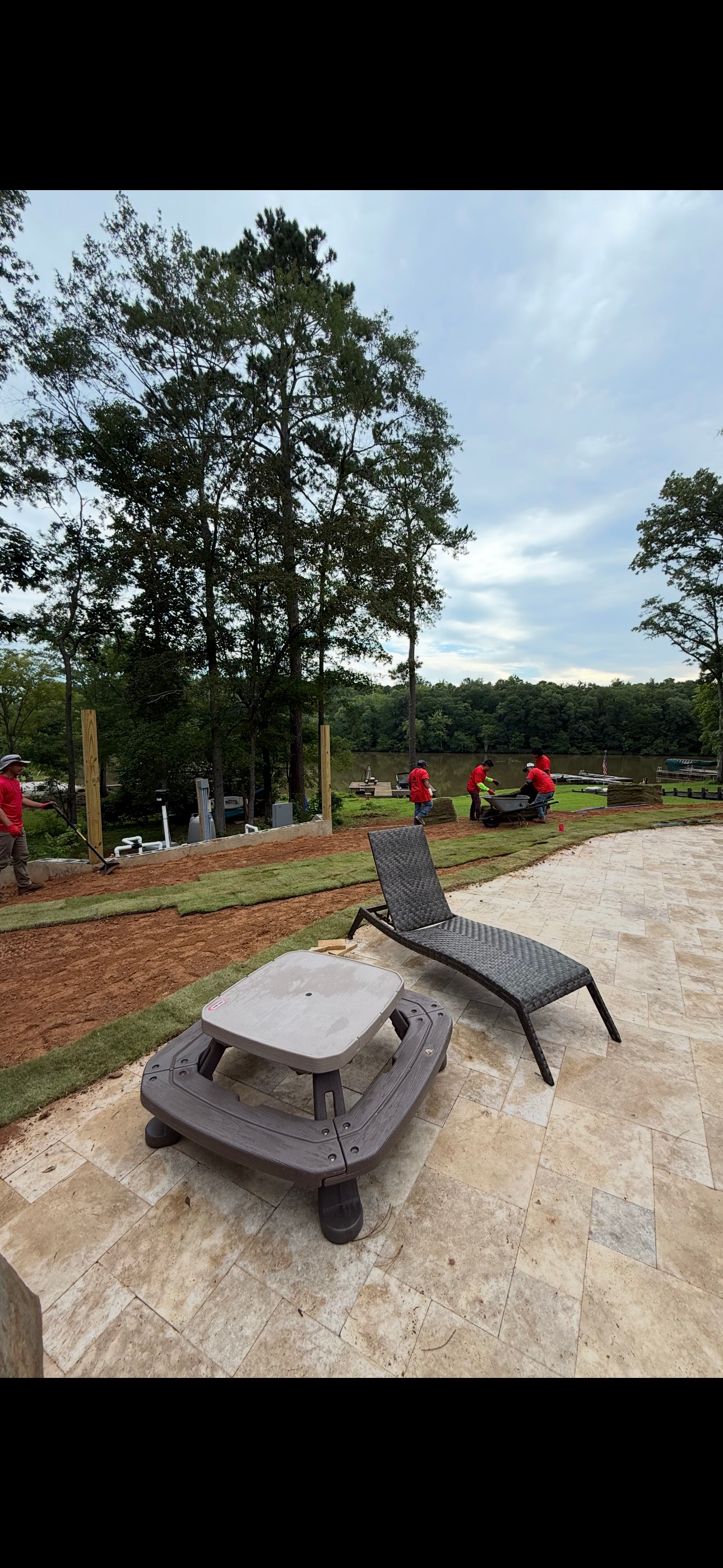 Workers installing a fence near patio furniture and trees on a cloudy day.