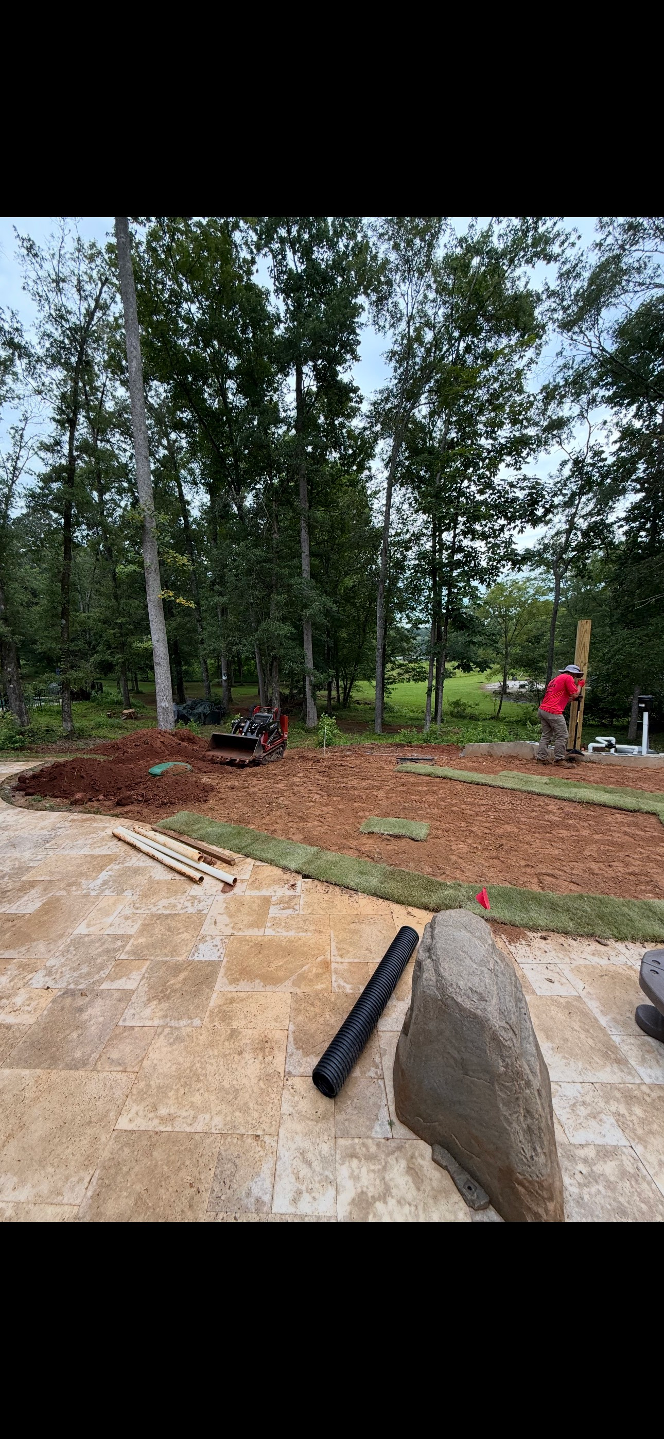 Landscaping in progress: Workers in a yard with trees in the background, surrounded by dirt and stone.