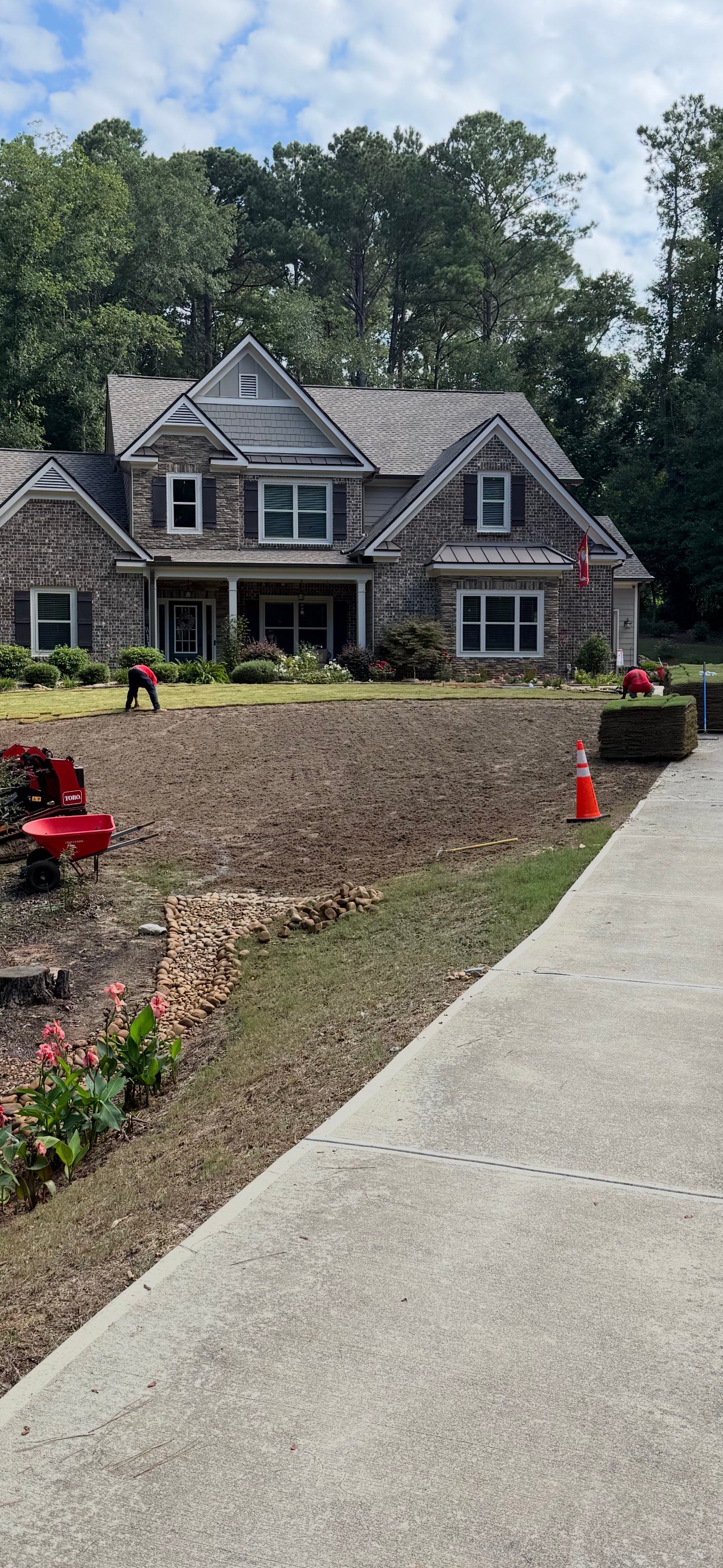 A large house with landscaping in progress; dirt area, concrete driveway, red equipment and greenery.