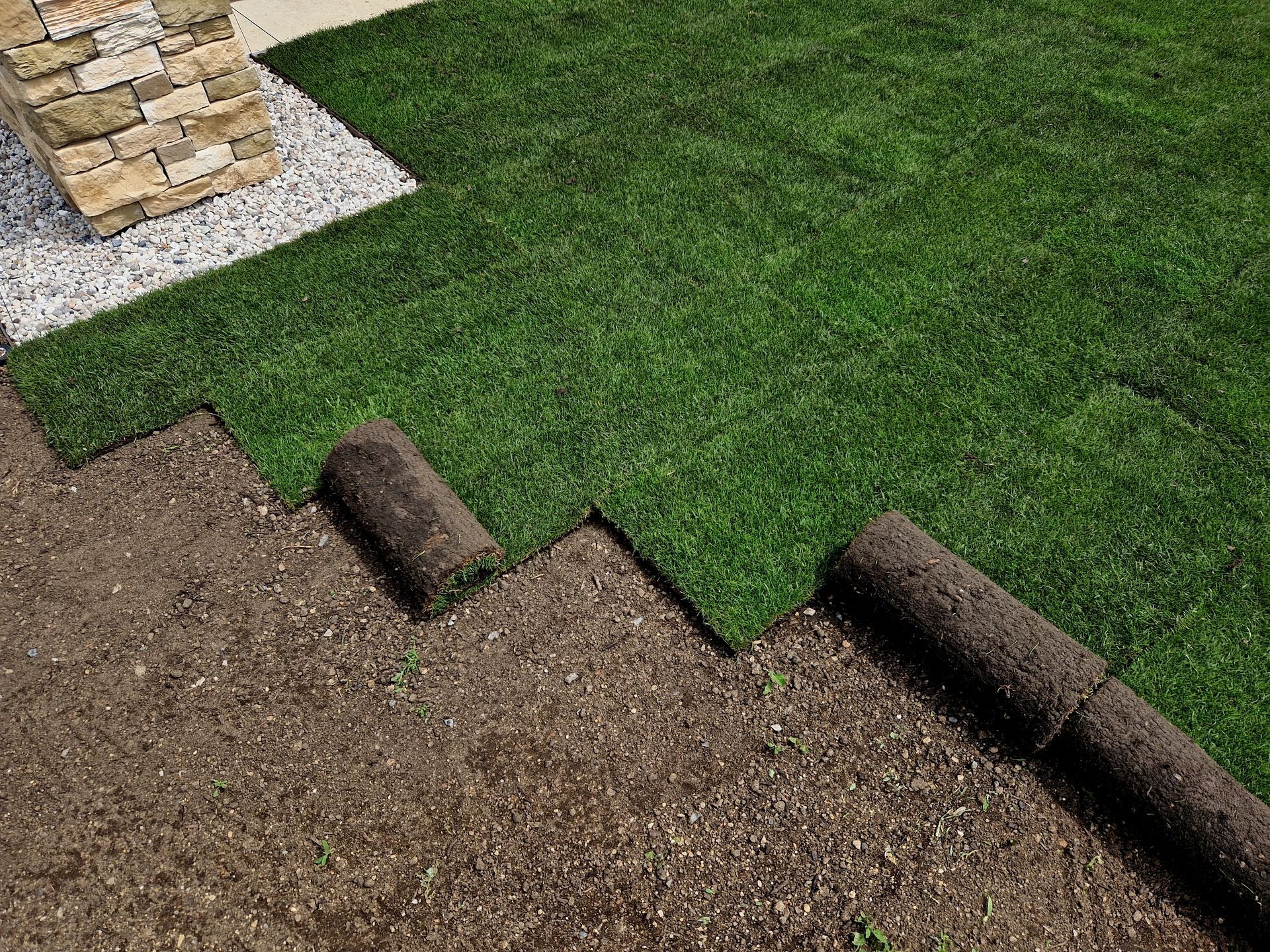A person in red walks in a yard undergoing landscaping, with mulch, sod, and trees in the background.