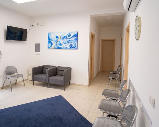 Una sala d'attesa medica ben illuminata, con sedie grigie, un tappeto blu e un corridoio che conduce alle porte interne.