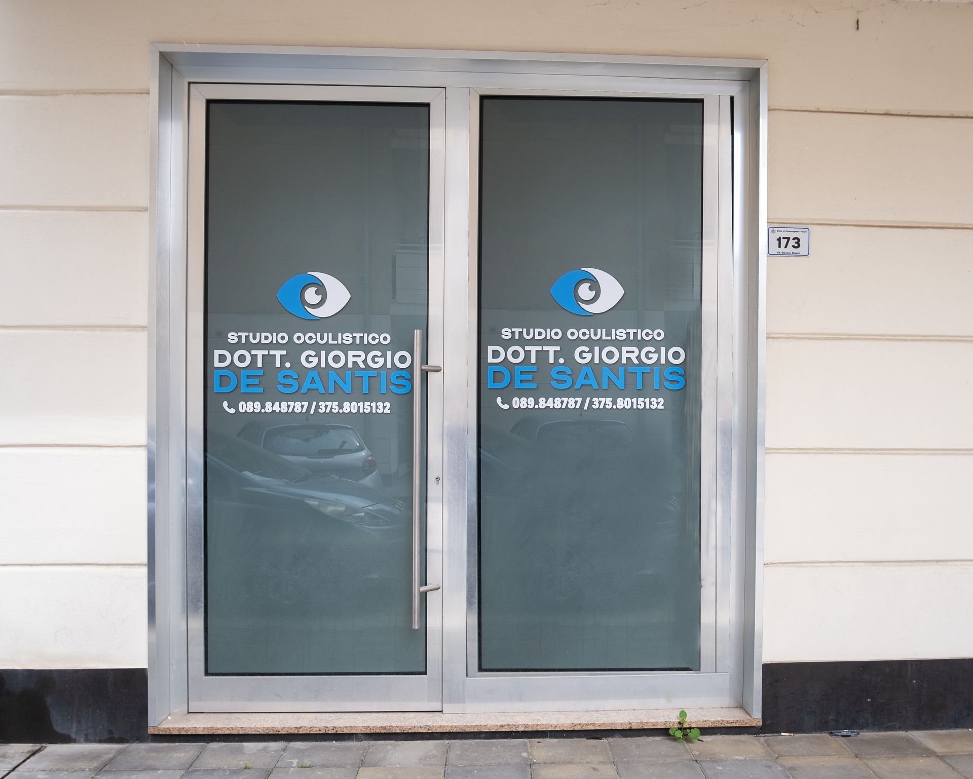 Doppie porte a vetri nello studio dell'oftalmologo Dott. Giorgio De Santis, con il logo di un occhio blu e il numero di telefono.
