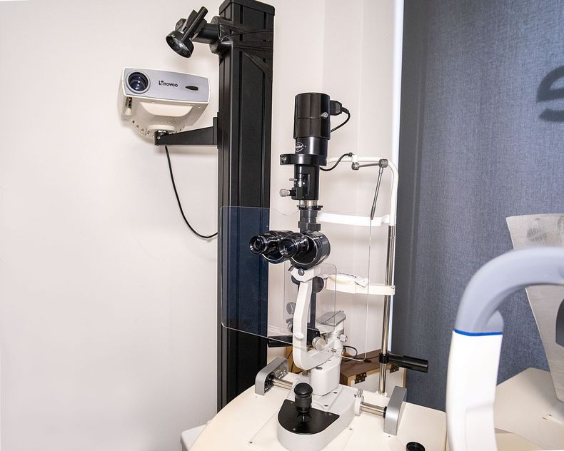 Un microscopio a lampada a fessura utilizzato per gli esami oculistici, posizionato su un tavolo in un ambiente d'ufficio.