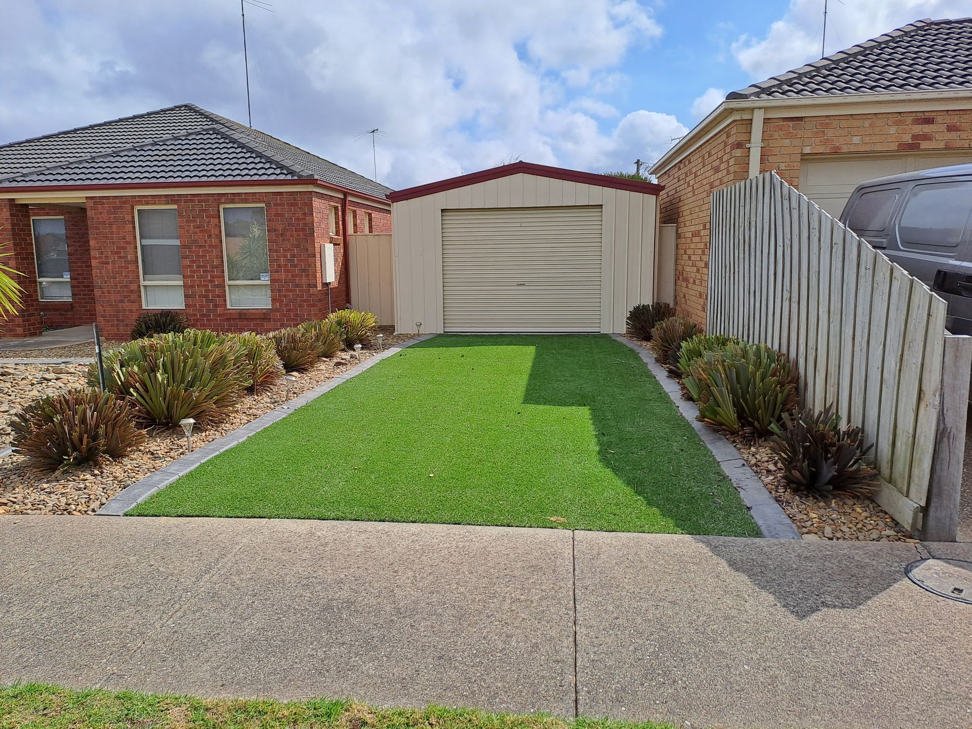 Front yard with bright green lawn leading to a single-car garage between brick houses