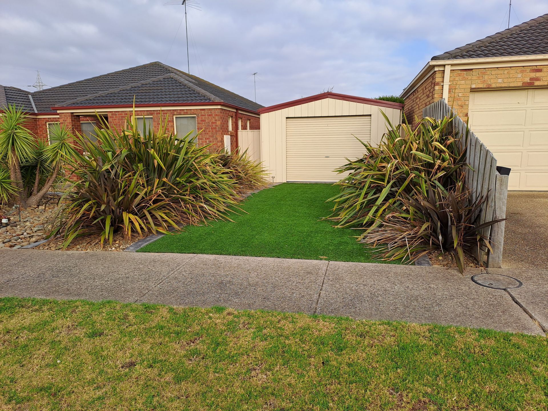 Suburban house front yard with green lawn, brick walls, and a garage under a cloudy sky