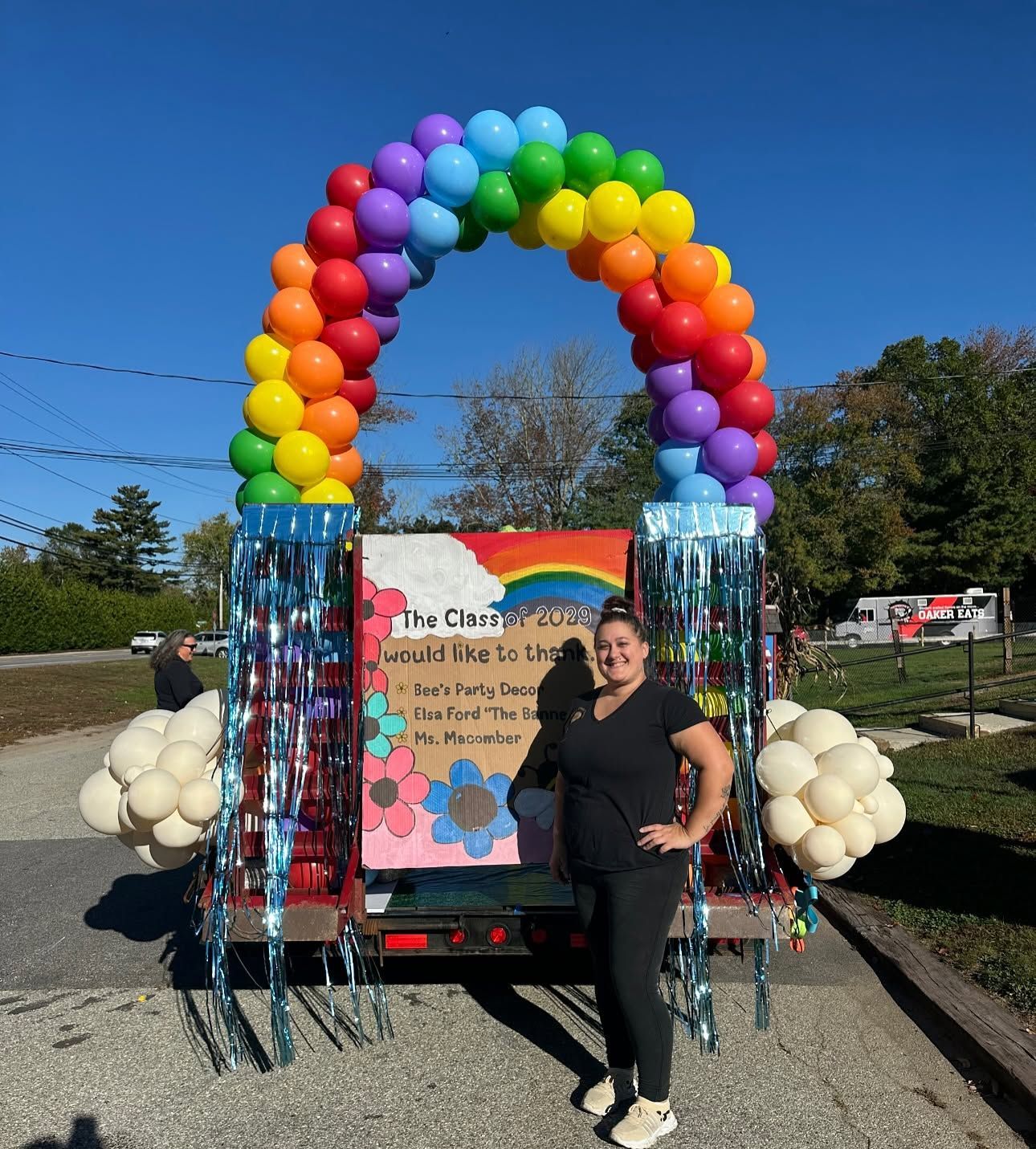 Person standing beside a rainbow balloon arch at an outdoor event display