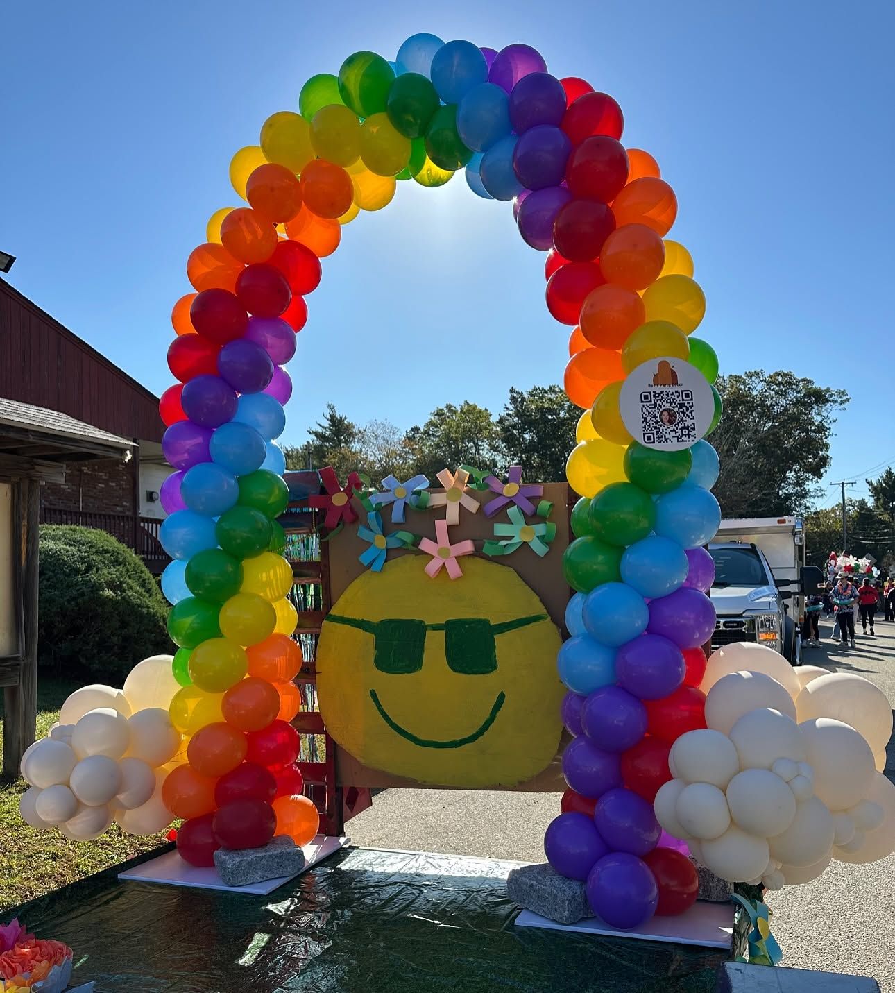 Rainbow balloon arch over a smiling sunflower decoration outdoors on a sunny day