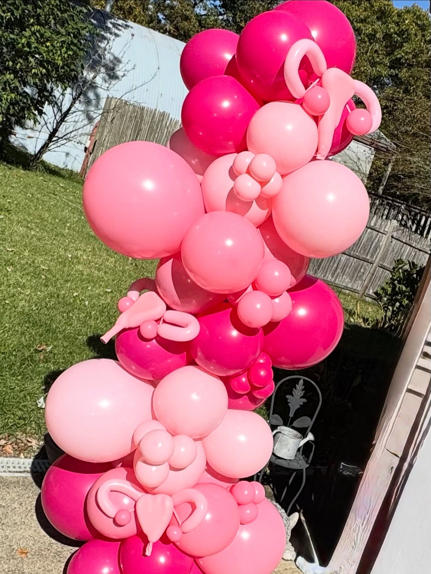 Pink balloon arch outdoors beside a glass door and grassy yard