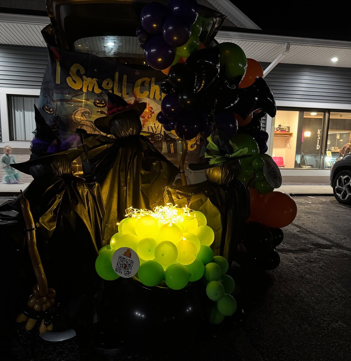 Halloween balloon display glowing under a porch with black, green, and orange balloons and a spider decoration