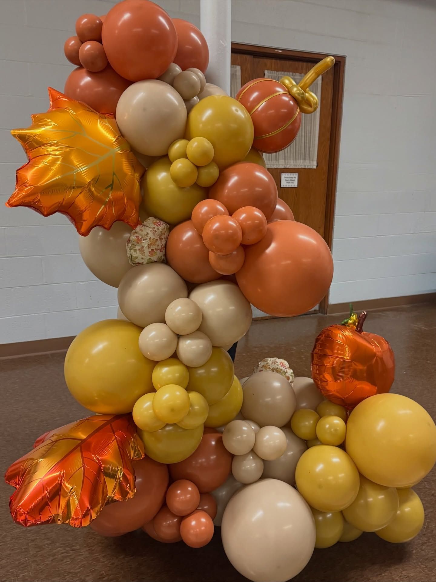 Autumn-themed balloon arrangement with orange, gold, and beige balloons on a stand