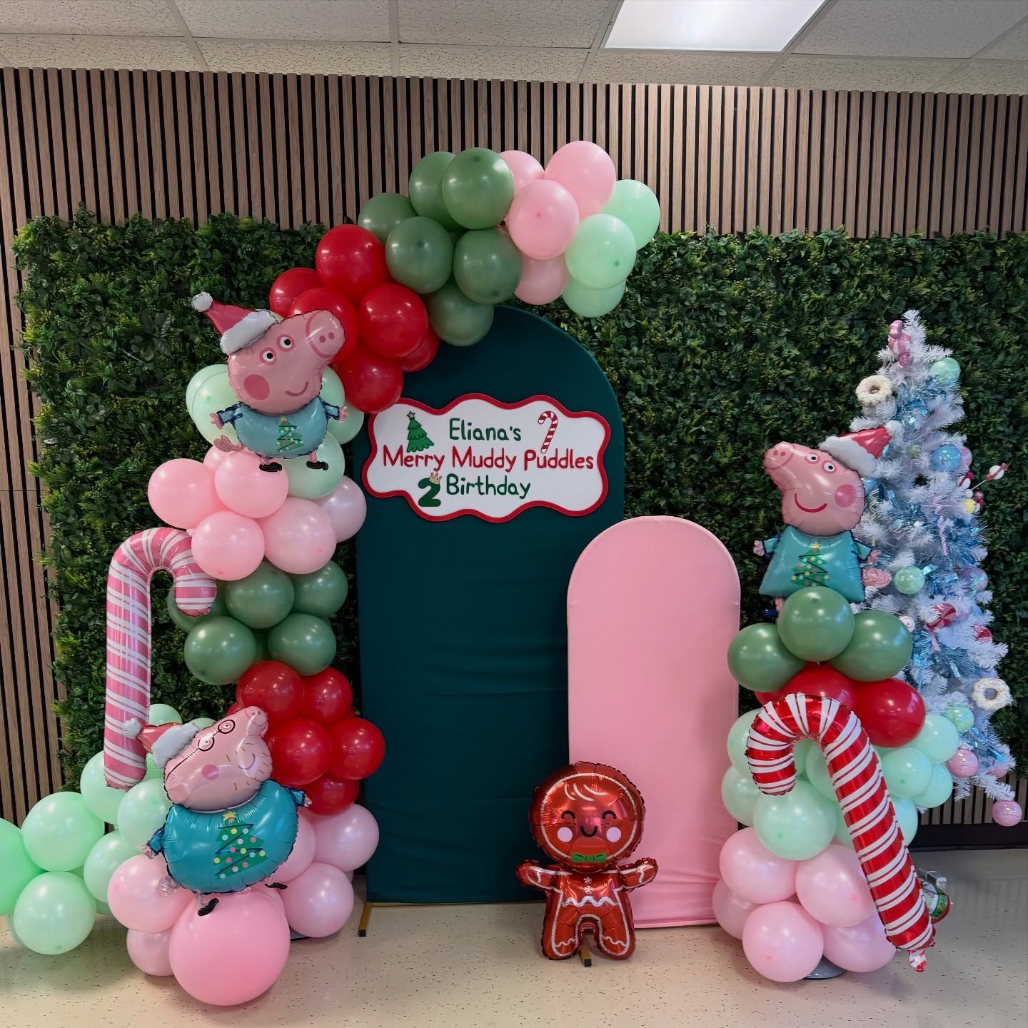 Peppa Pig-themed birthday balloon display with pink, green, red, and blue arches and a small gingerbread figure.