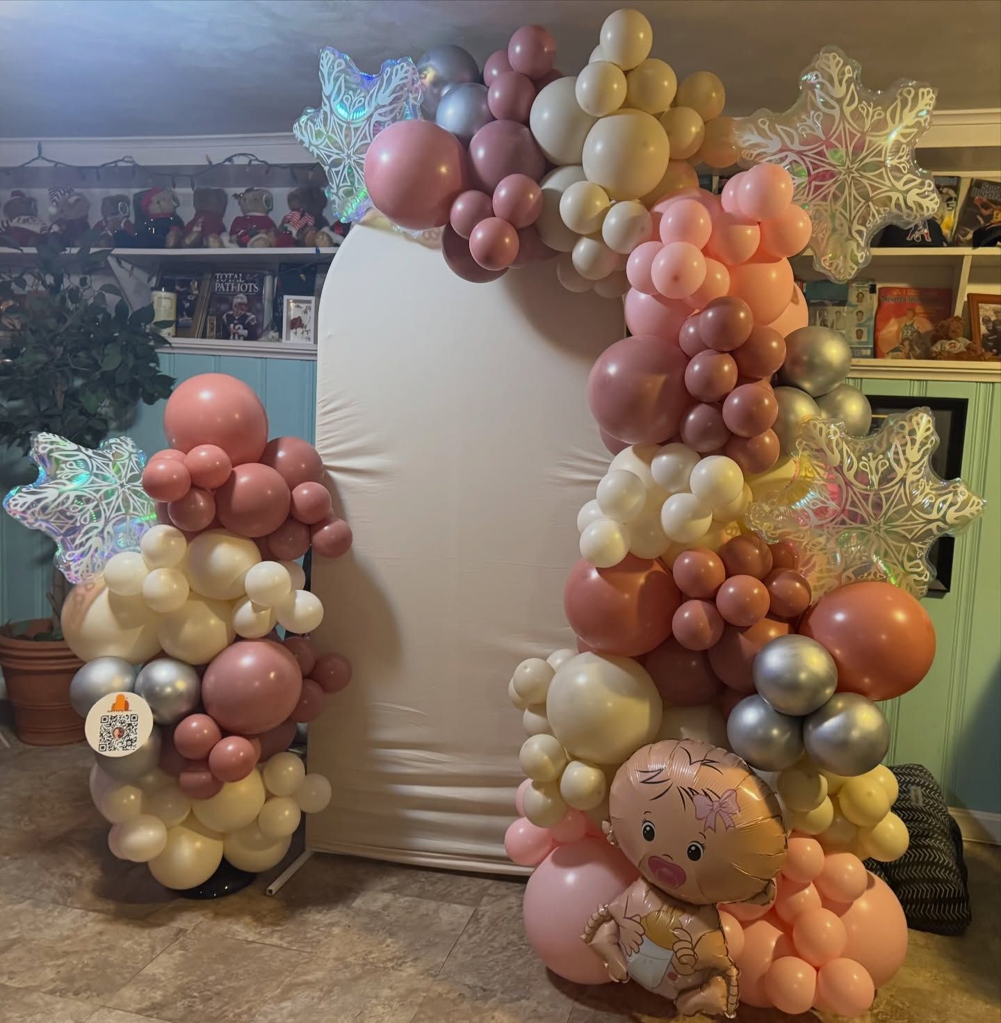 Large balloon arch in blush, gold, and silver around a blank white backdrop, with star balloons and a teddy balloon.