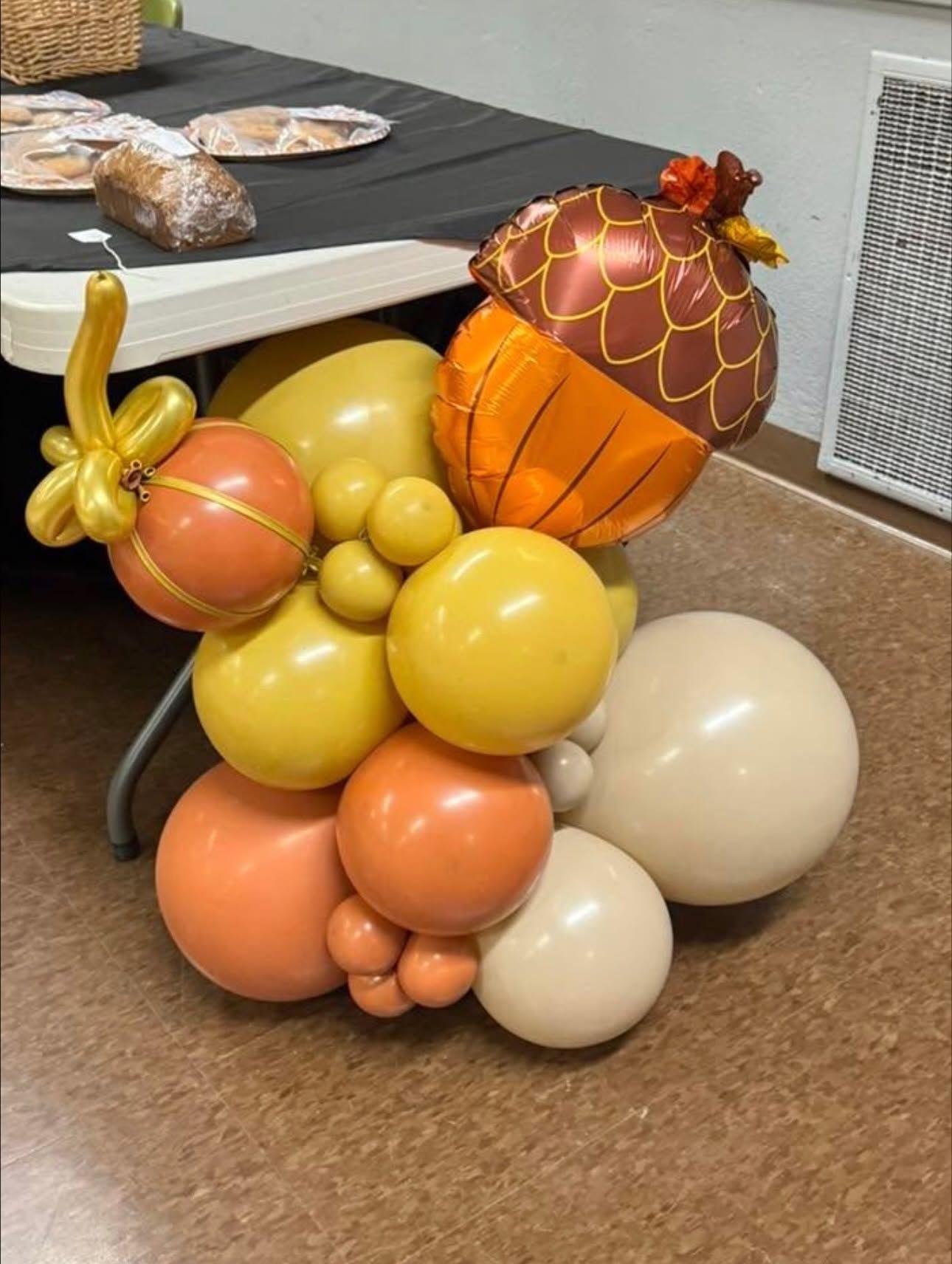 Autumn balloon arrangement in orange, yellow, and cream beside a table indoors