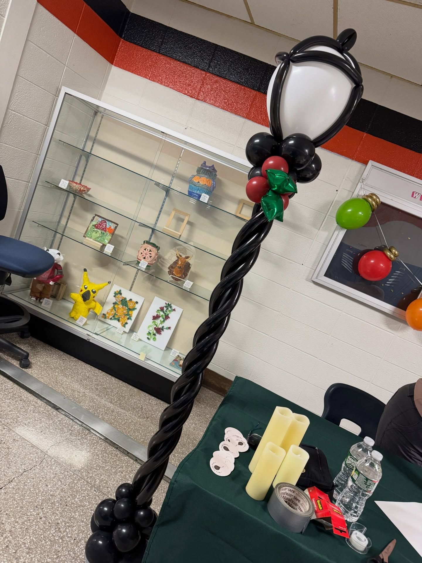 Indoor display with a black twisted pole, balloon decorations, and a glass case of toys in the background