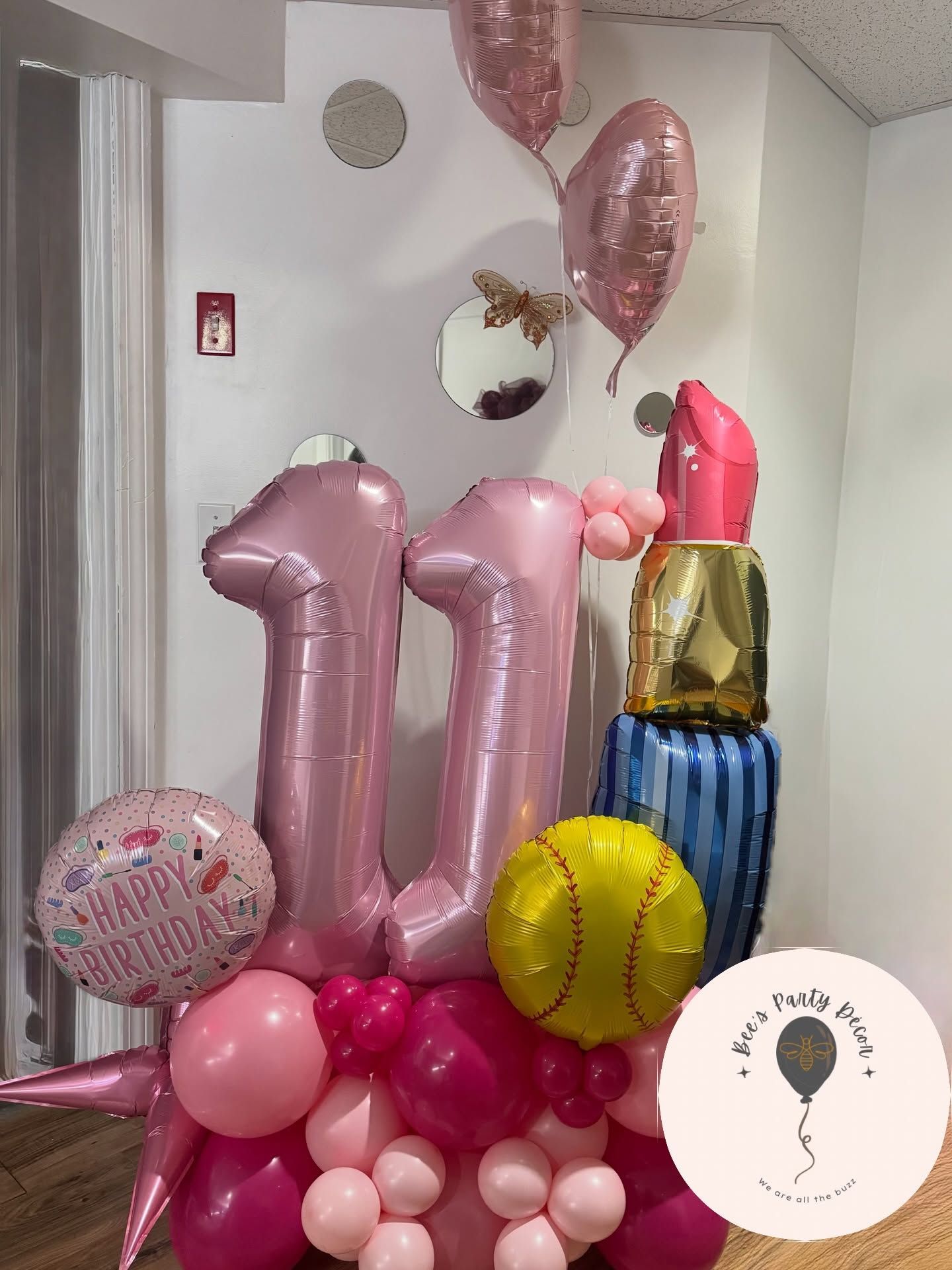 Pink balloon display with large “11” and “U” numerals, balloons, and a cake stand in a decorated room