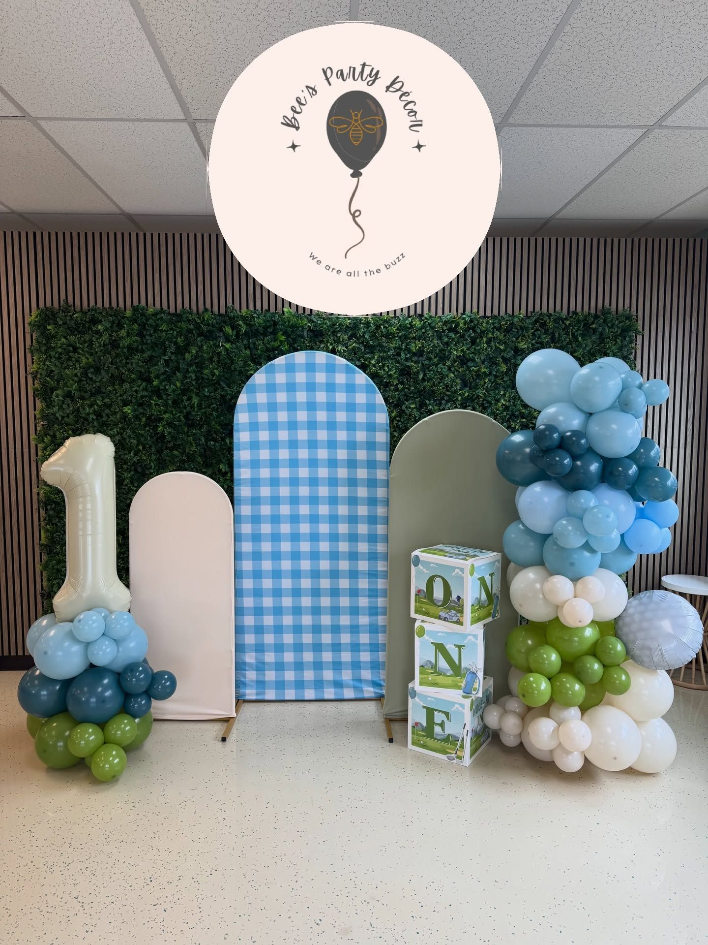Balloon-decorated party backdrop with blue, white, and green arch panels and a circular sign above.