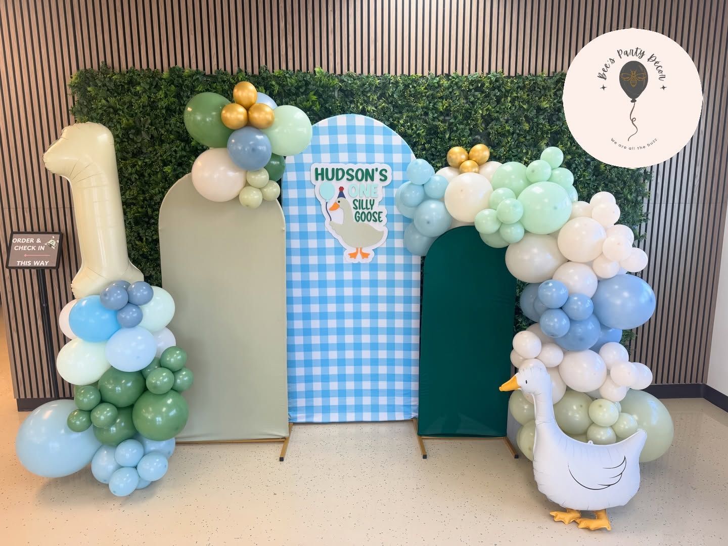 Pastel balloon arch around blue checkered “Hudson’s” backdrop with oversized one on the left and white buckets on both sides