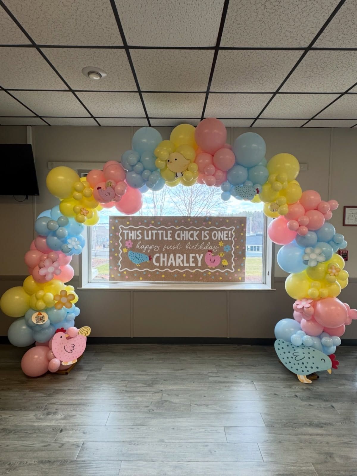 Pastel balloon arch around a “This little chick is one” birthday sign in a room