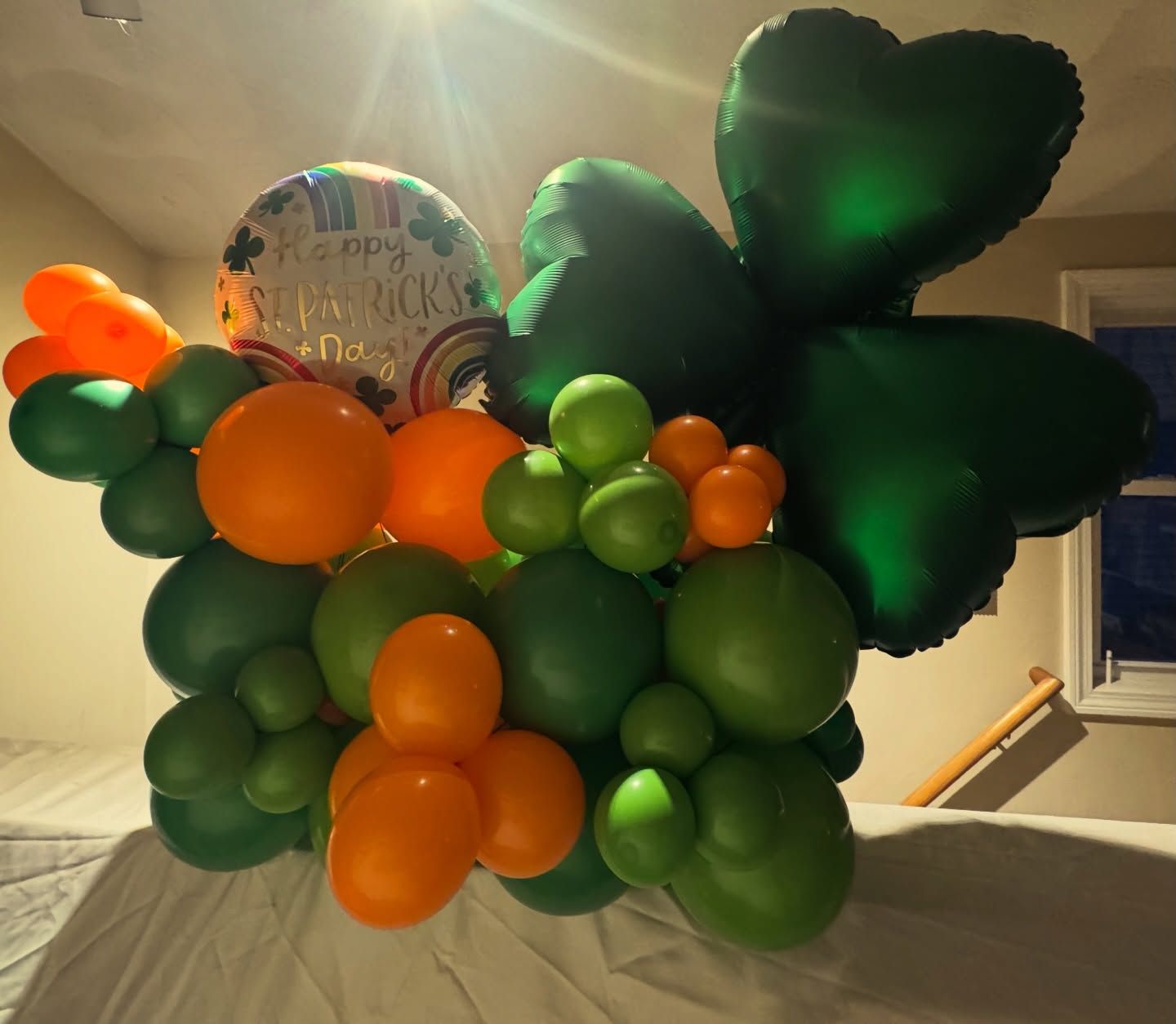 Green, orange, and black balloon bouquet with a Halloween-themed balloon in a warmly lit indoor stairwell.