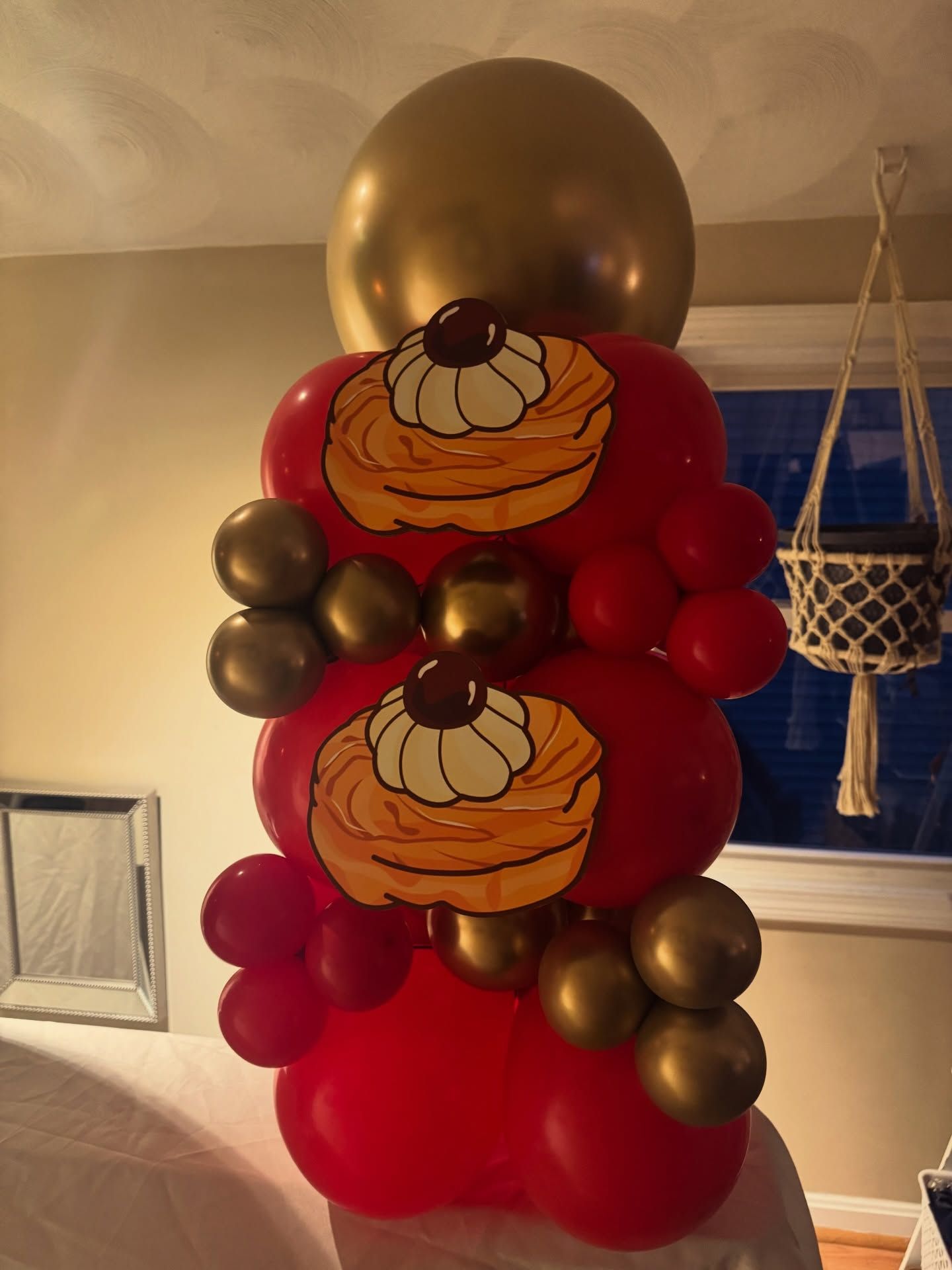 Red and gold balloon column with cupcake decorations and a large gold balloon top indoors.
