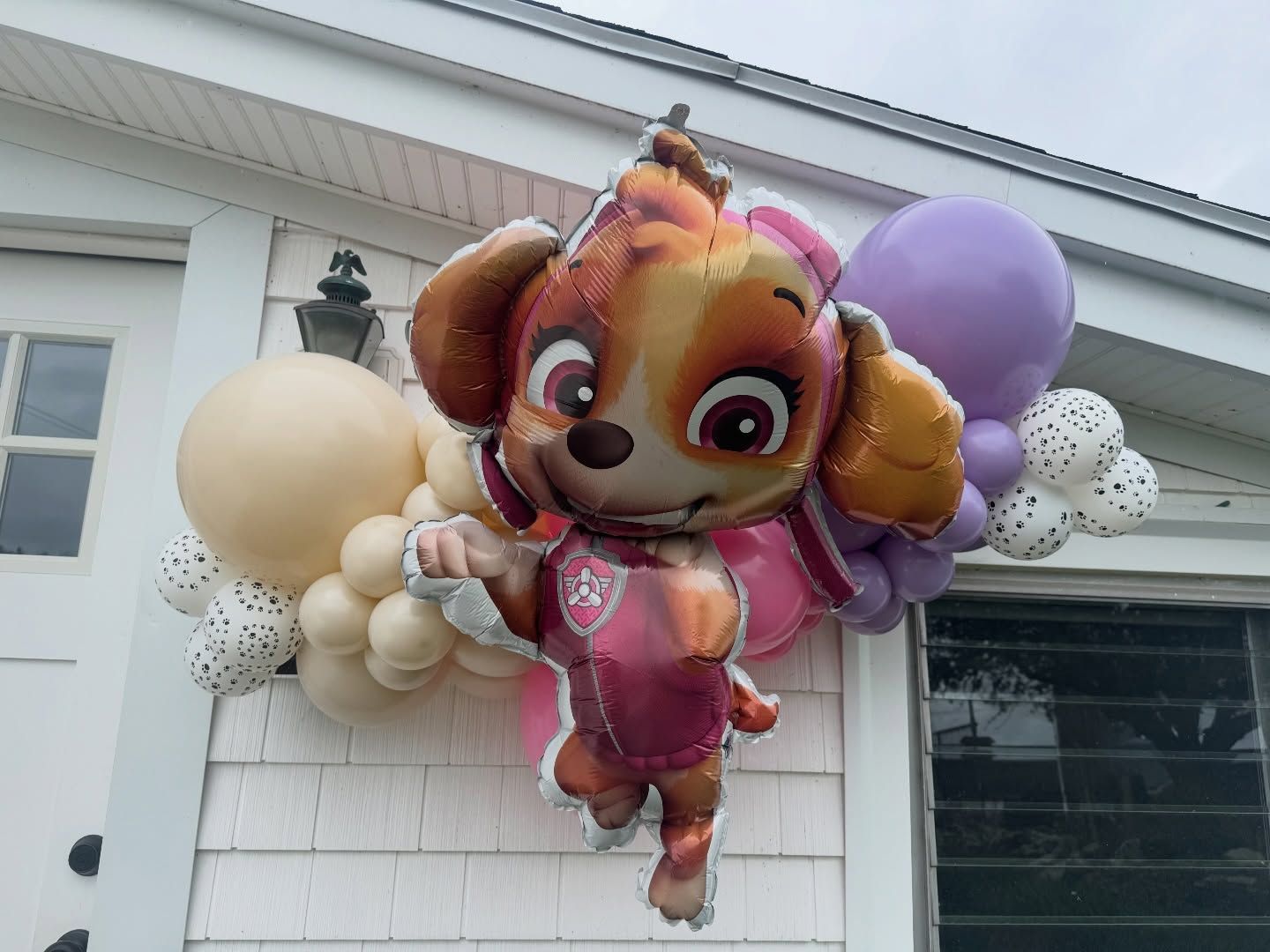 Paw Patrol Skye balloon display hanging outside a house with cream and purple balloons