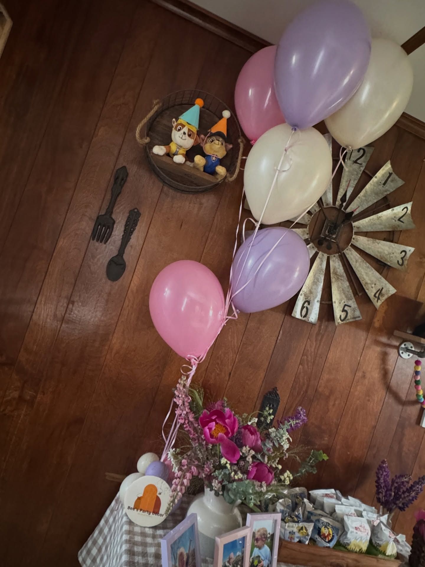 Birthday decor with pastel balloons, flowers, and a wall fan in a wood-paneled room