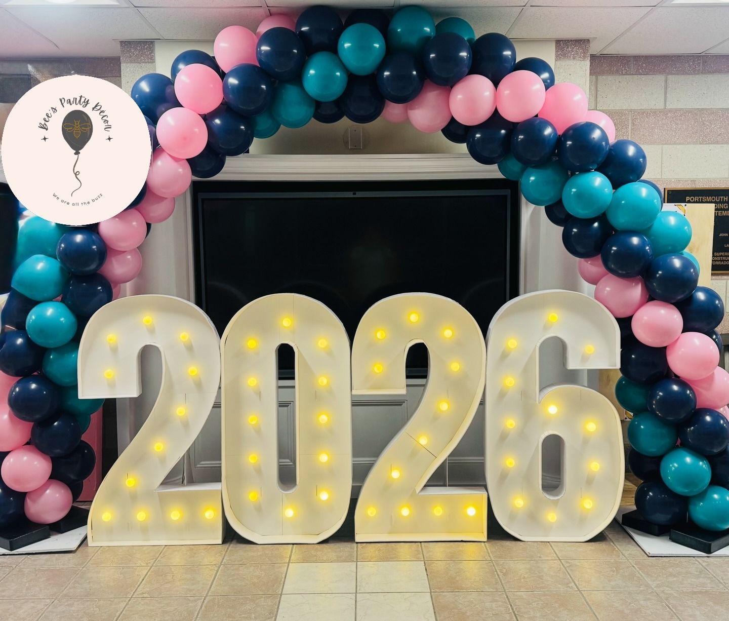 2026 marquee letters with lit bulbs, framed by pink and blue balloons in a festive arch