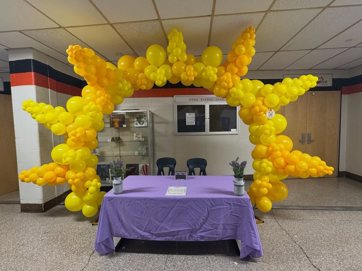 Yellow balloon star arch over a purple-covered table in an indoor lobby area