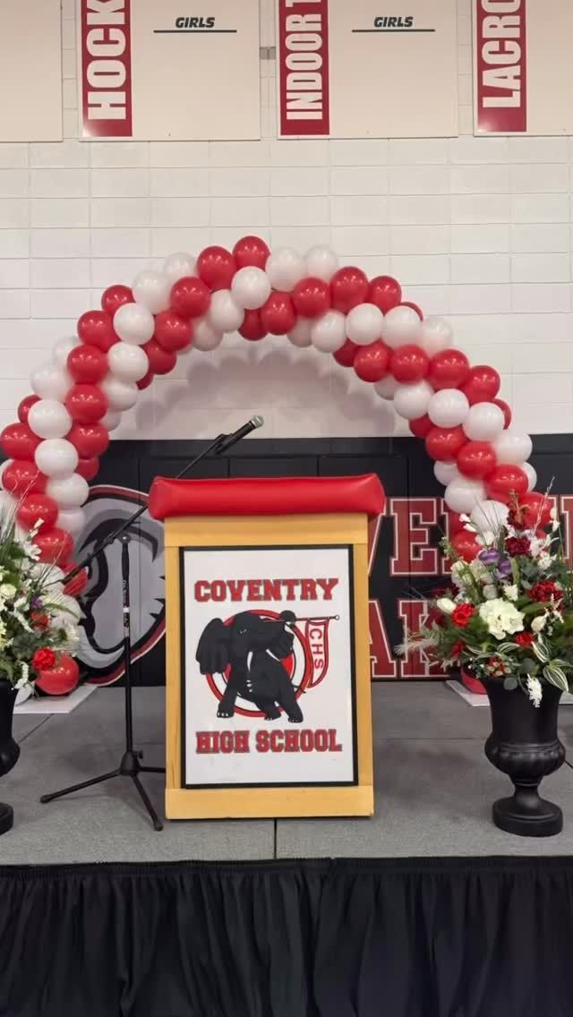 Coventry High School podium with red-white balloon arch and floral arrangements on stage