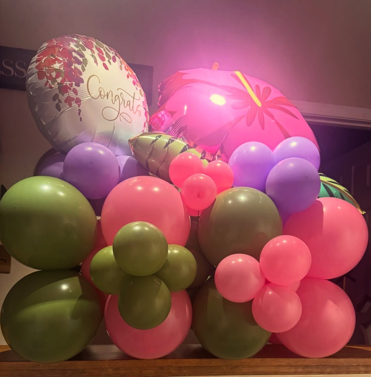 Colorful balloon bouquet with pink, purple, green, and red balloons in an indoor setting