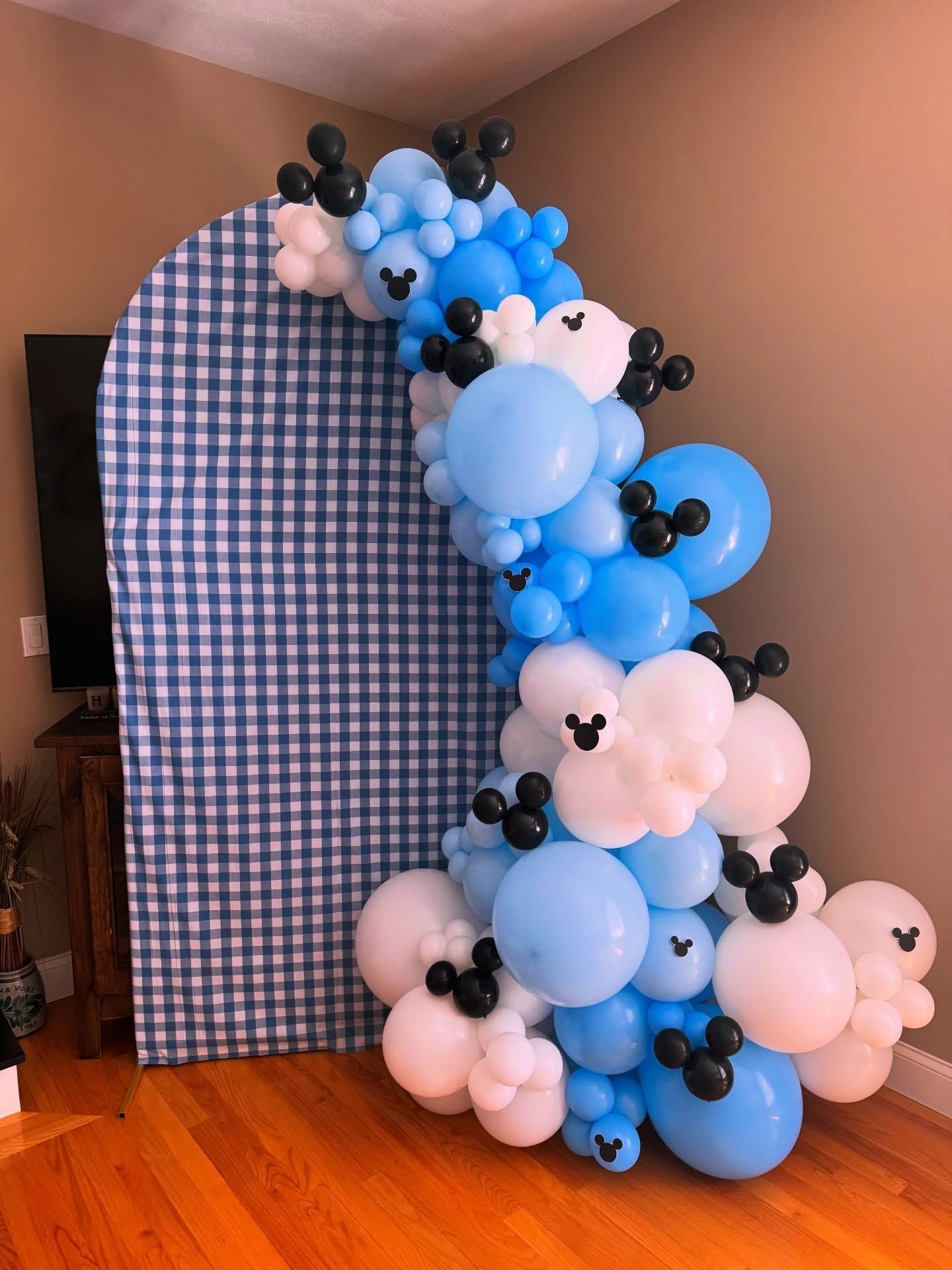 Blue, white, and black balloon arch beside a blue gingham photo backdrop in a room.