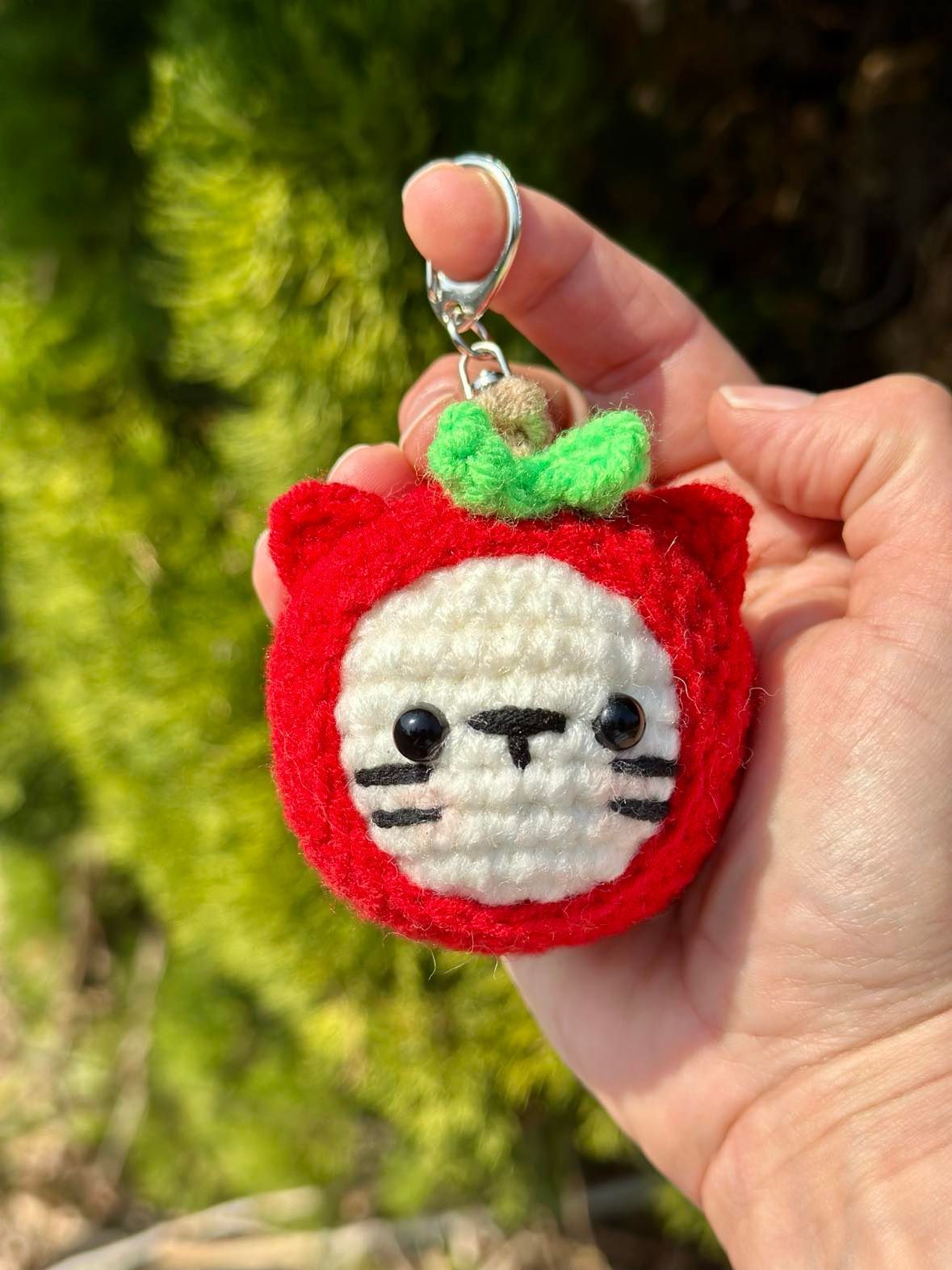 Hand holding a red and white cat-shaped keychain with green leaf top.