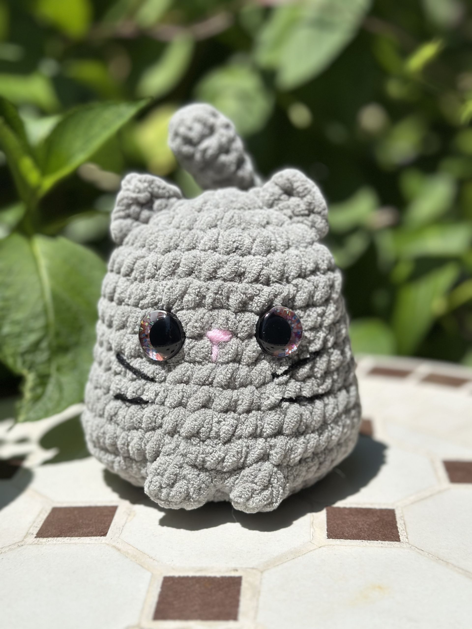 Crocheted gray cat toy with large black eyes, pink nose, and whiskers, held in a hand.