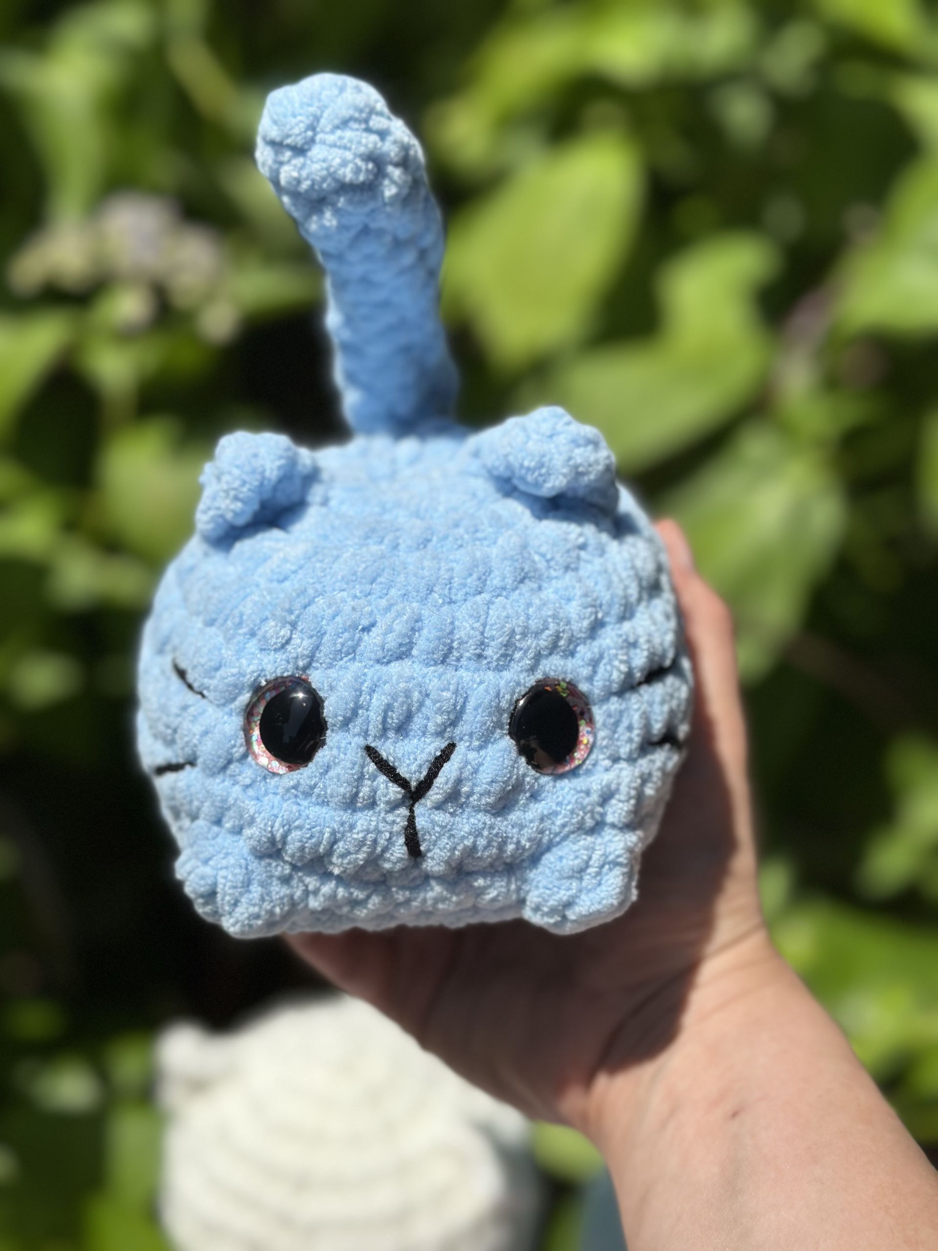 A small, light-blue crochet cat held in hand, with black eyes and upright tail.