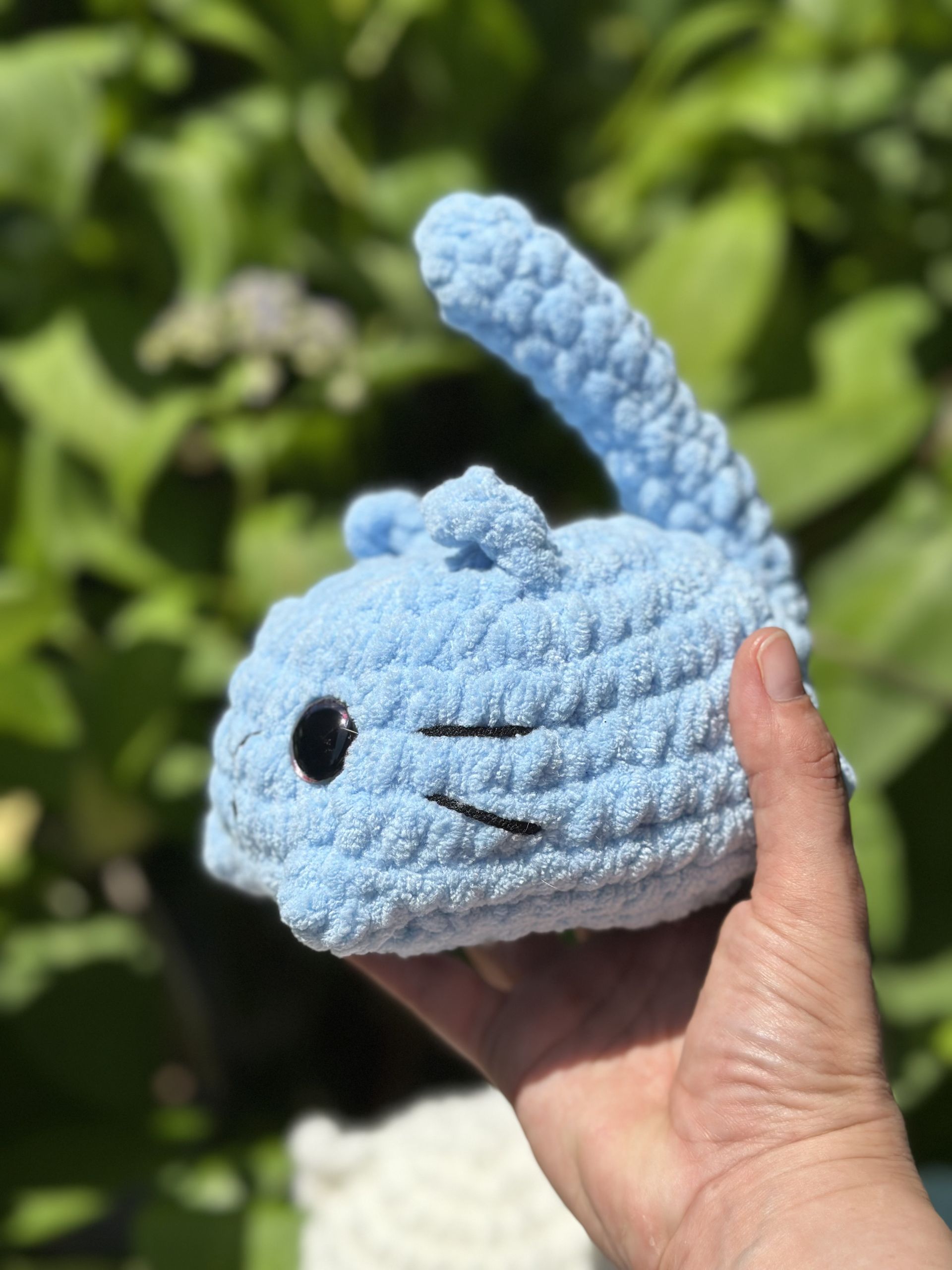 A small, light-blue crochet cat held in hand, with black eyes and upright tail.