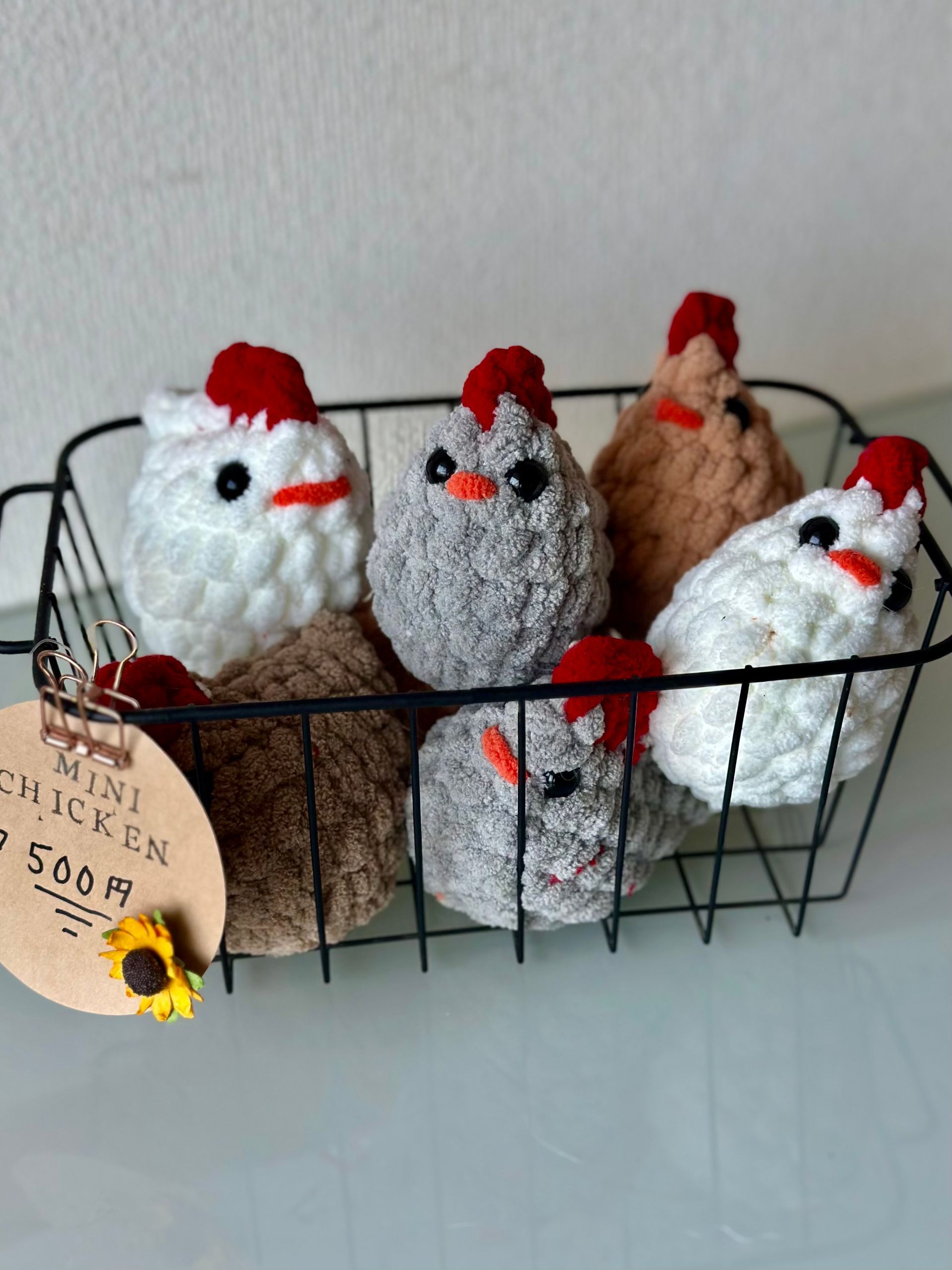 Handmade crochet chickens in a wire basket; various colors, red combs, price tag.