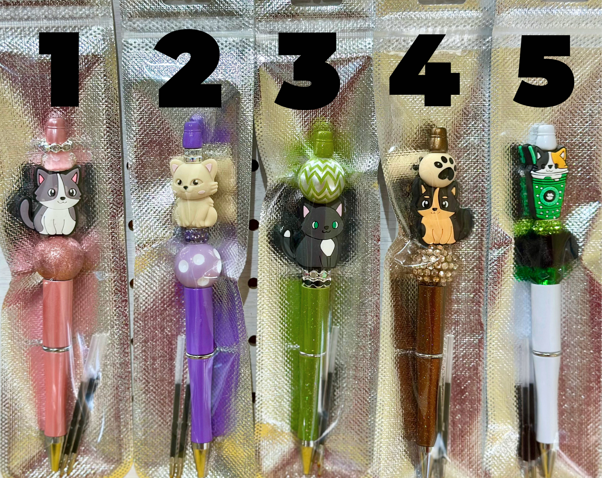 Five colorful pens, each with unique decorative tops, in clear packaging.