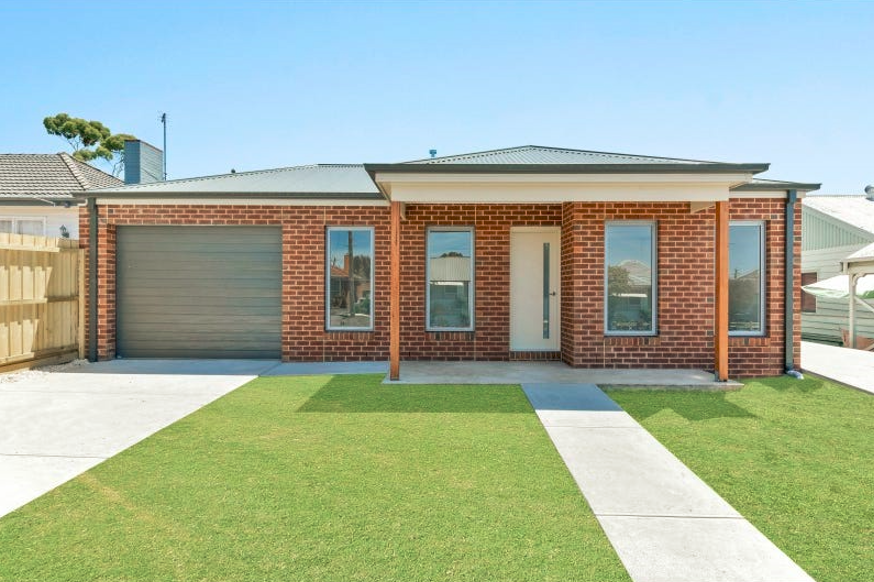 Brick house with garage, front porch, and green lawn under a clear blue sky.