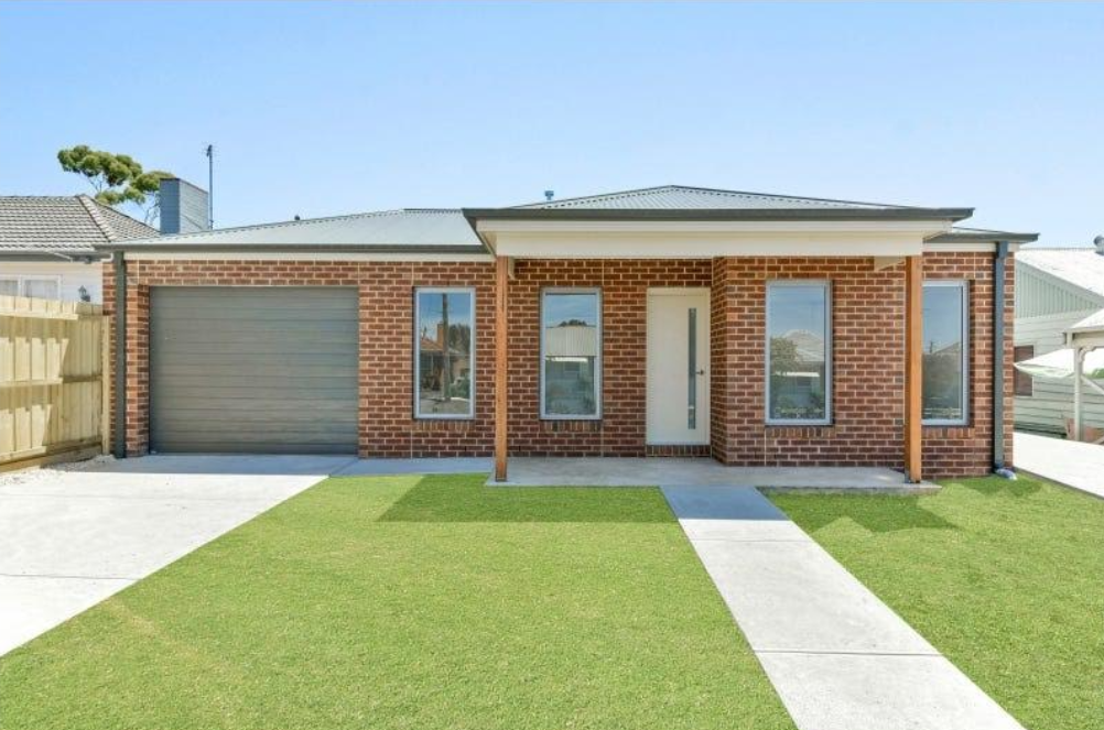 Brick house with garage, green lawn, concrete path, and blue sky.