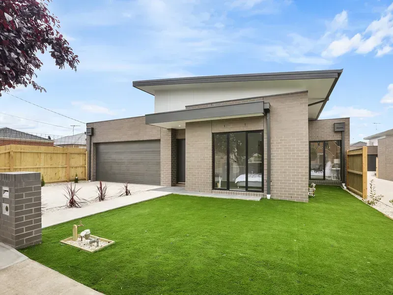 Modern house with grey brick facade, green lawn, and garage door under a blue sky.
