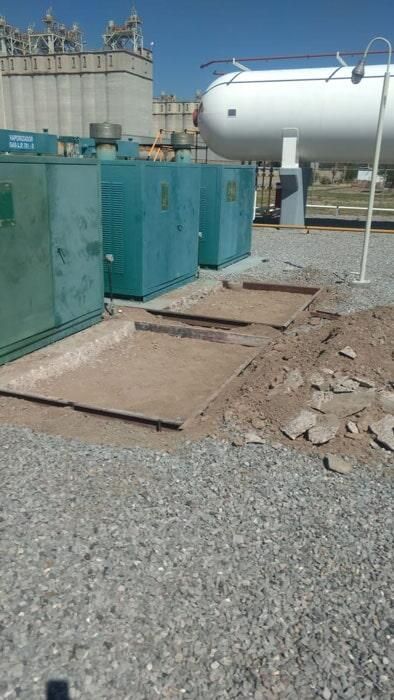 Un gran tanque blanco está al lado de una fila de contenedores azules.