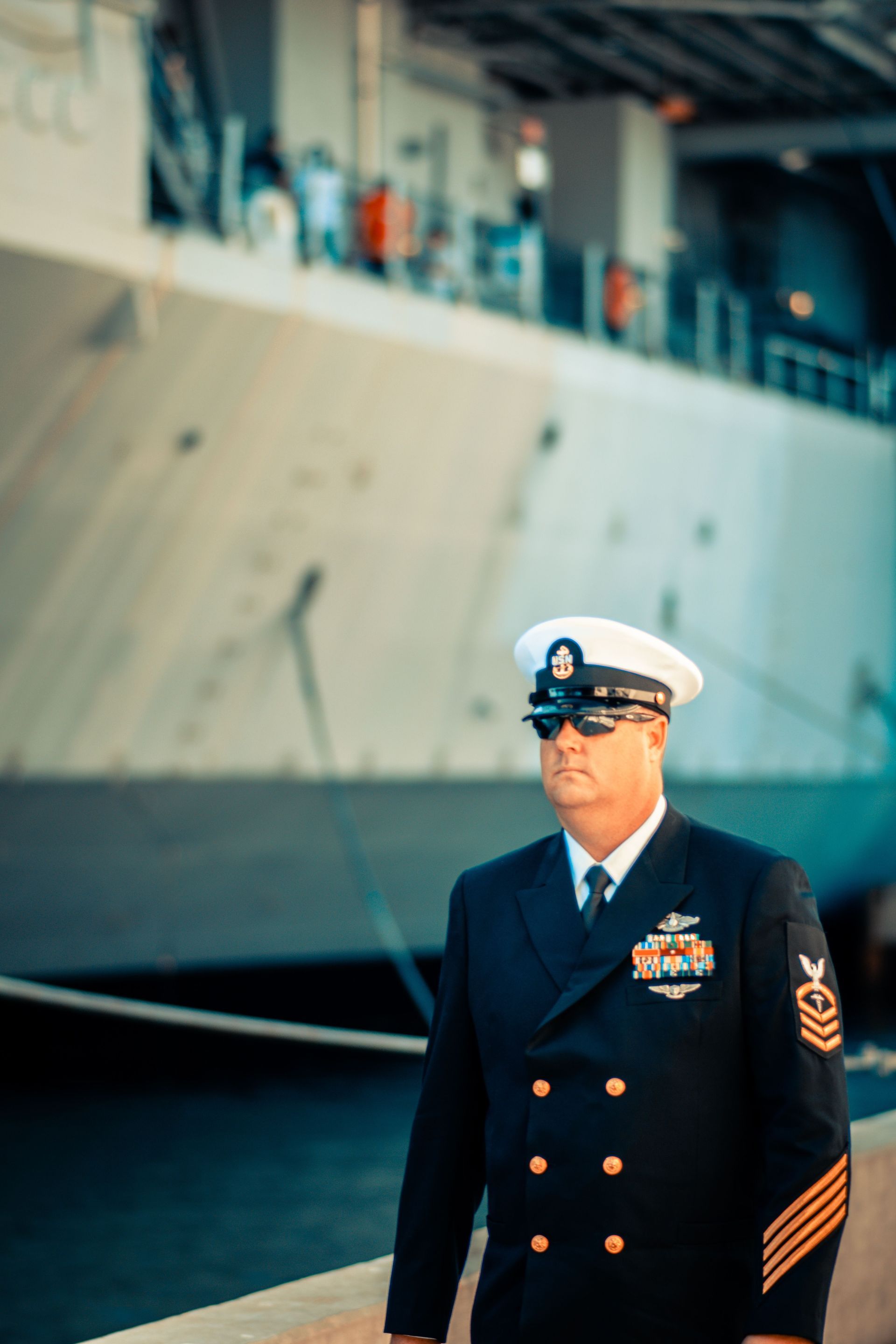 Navy officer in dress uniform standing before a docked warship
