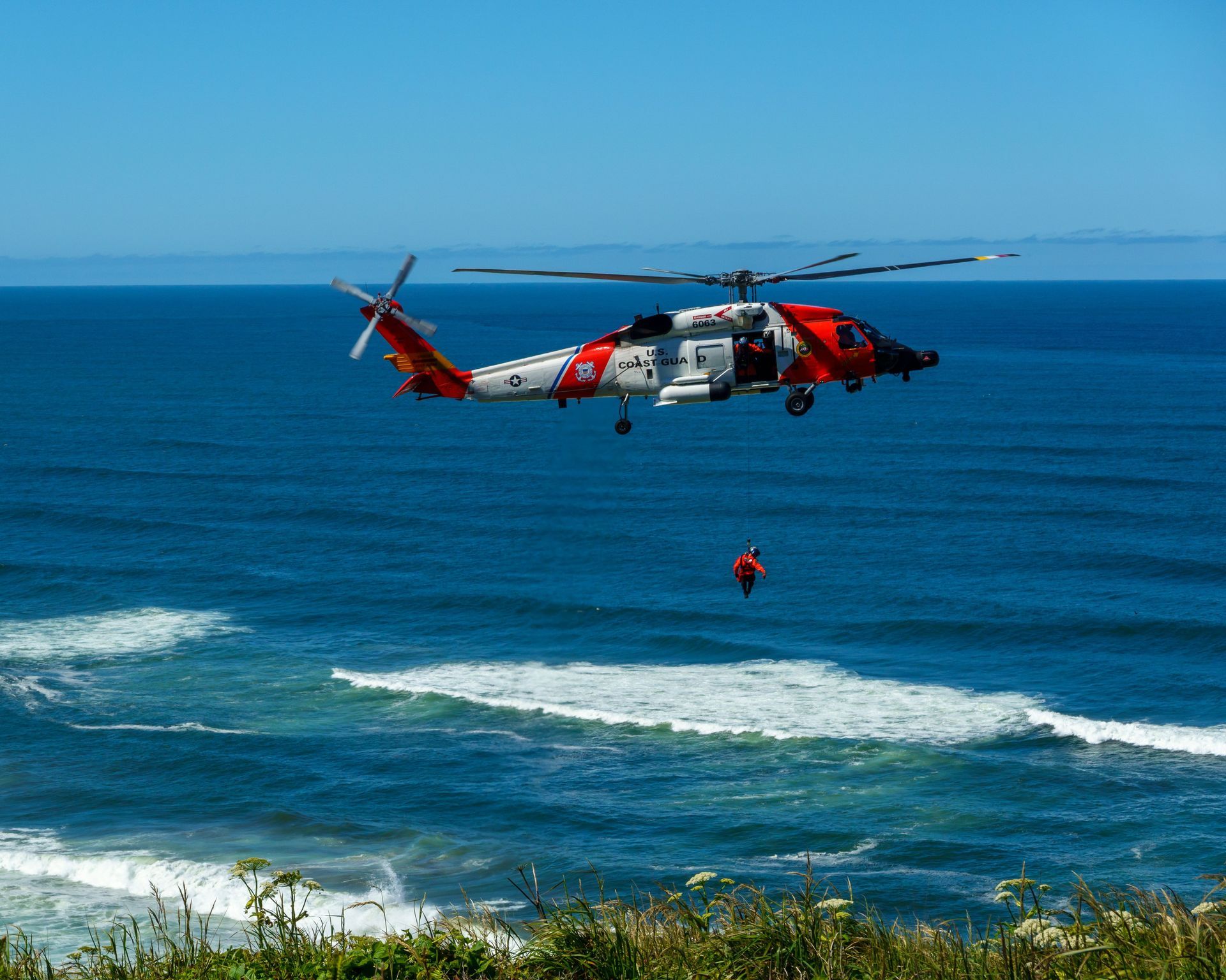 Red-and-white helicopter hovering over the ocean with a person suspended below it