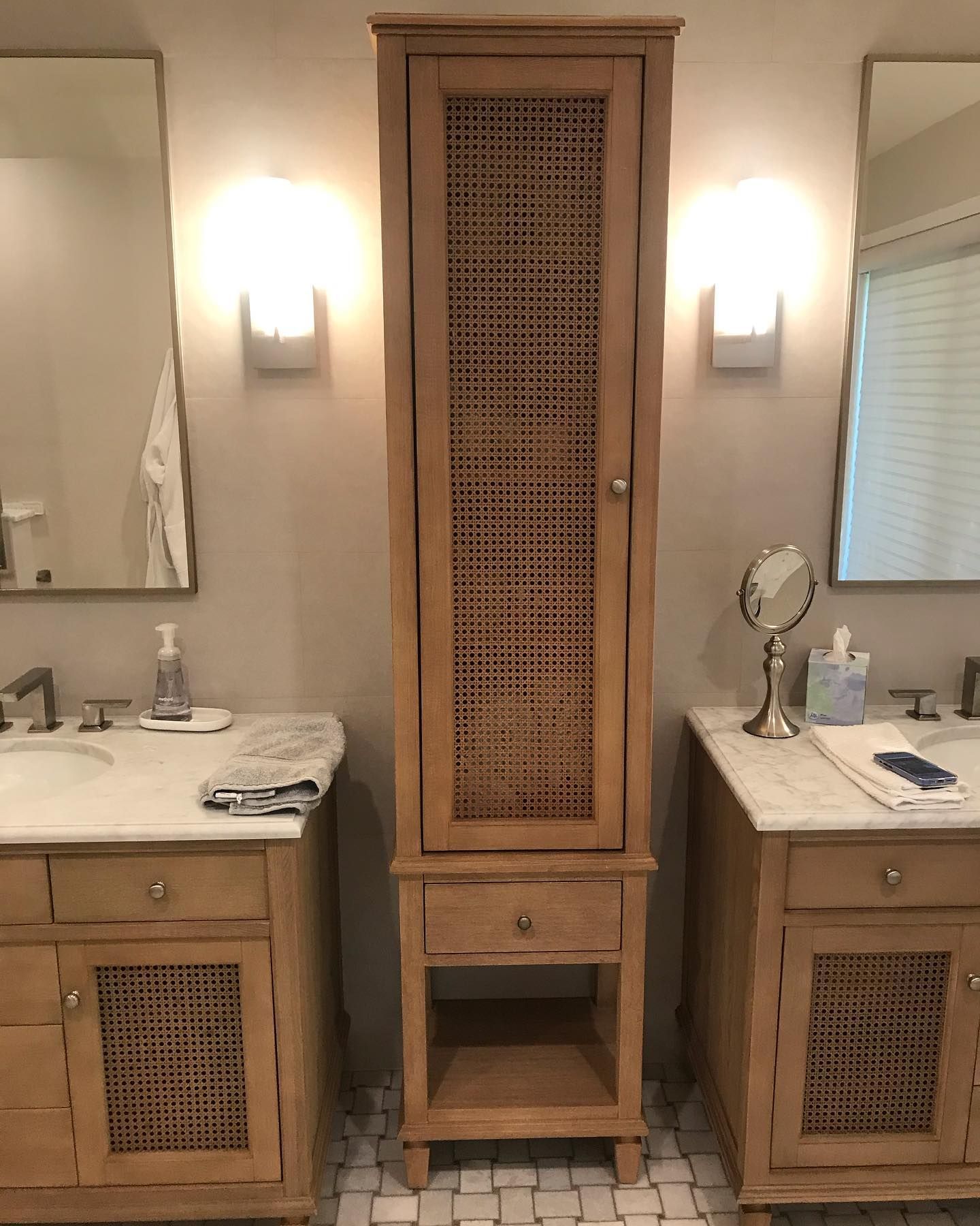 A wooden bathroom vanity with a central tall cabinet featuring cane-patterned doors, flanked by two sinks with mirrors.